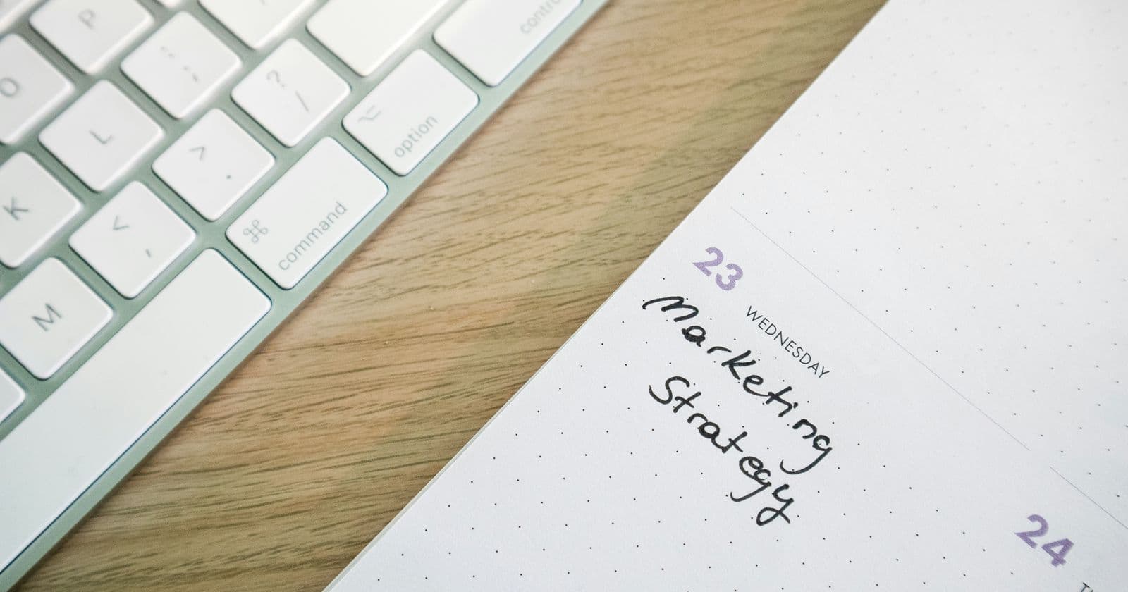 Stock photo: Spiral planner page headed Marketing Strategy lying on a light wooden desk beside a white keyboard